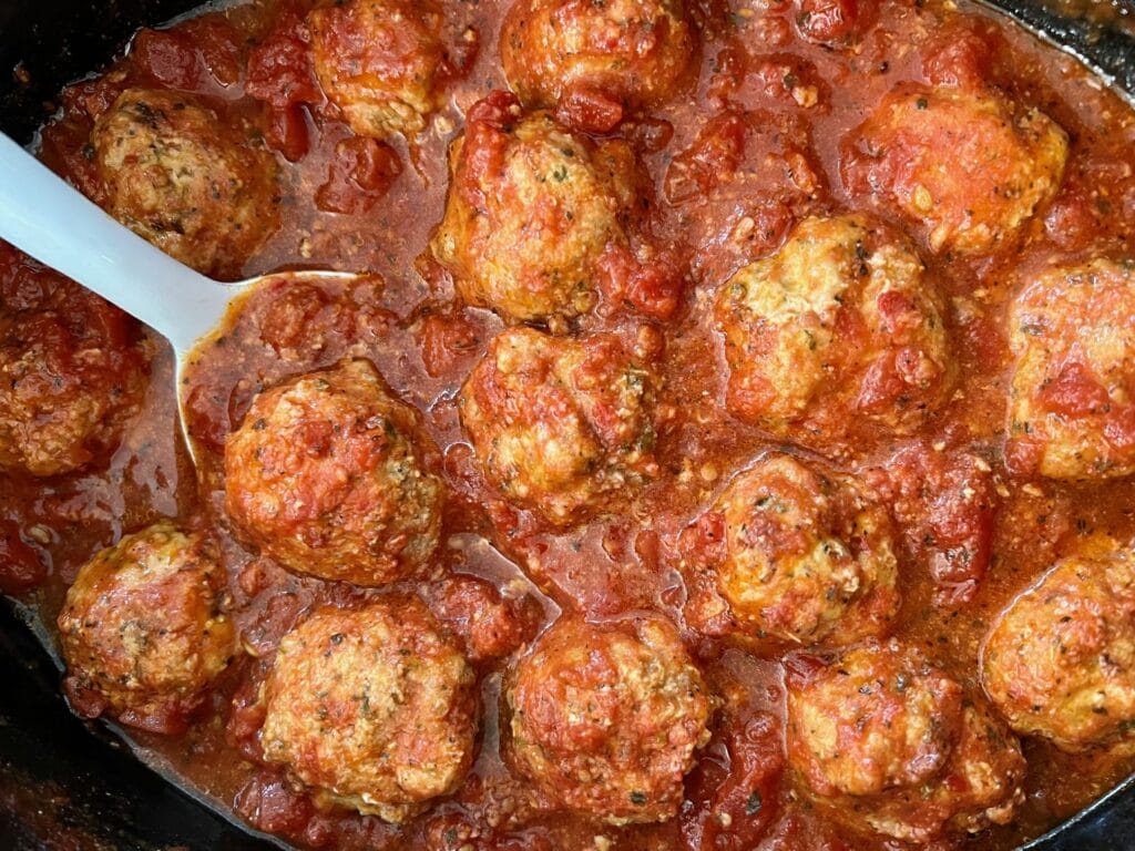 Turkey meatballs in a slow cooker with a white spoon