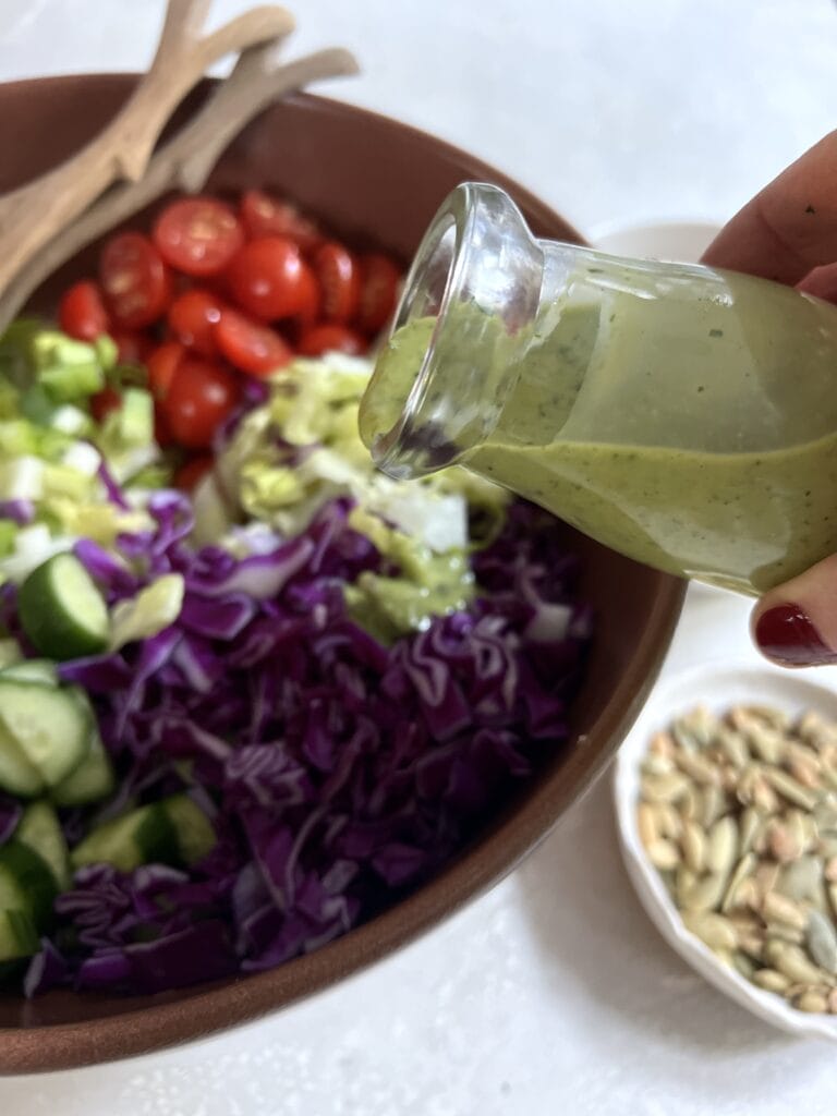 Pouring creamy cilantro dressing over chopped salad